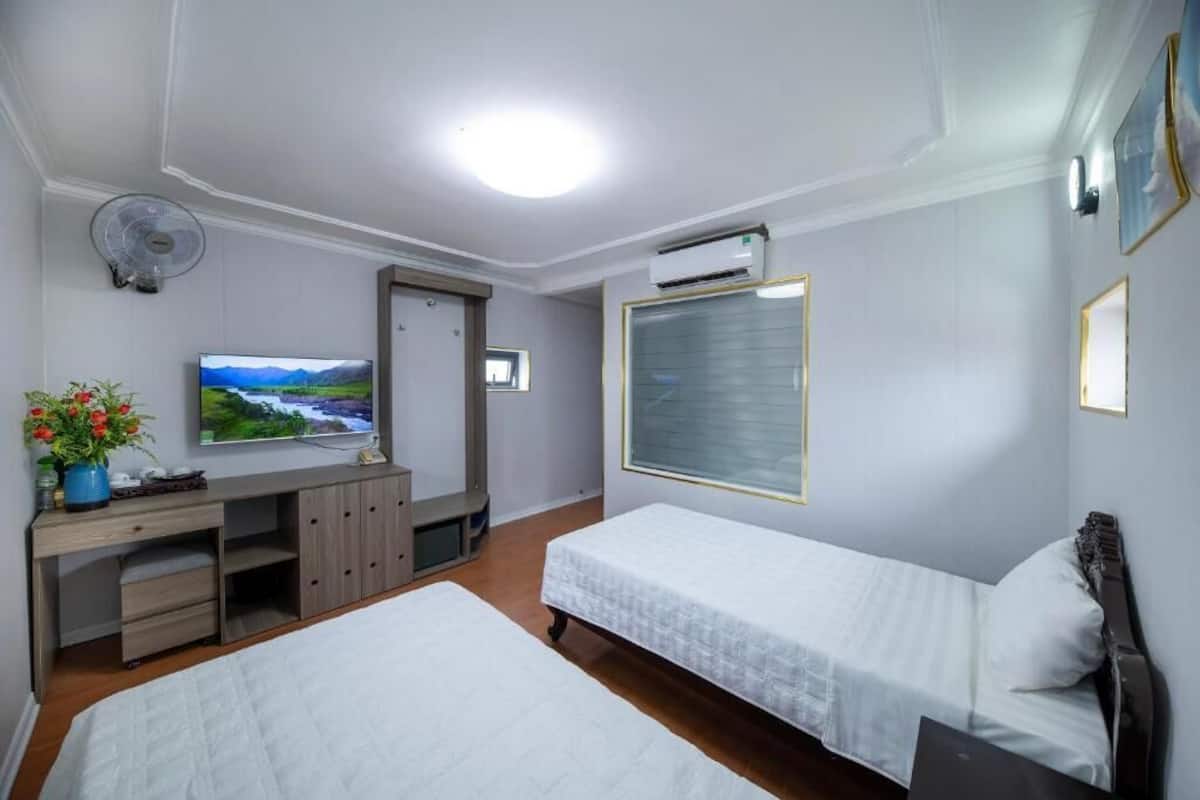 A hotel room with two beds, a TV, a desk with a computer, a fan, and an air conditioning unit.