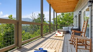 Una terraza de madera con pérgola, mobiliario exterior y vistas a montañas.