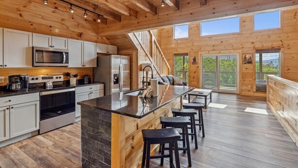 Una cocina amplia con electrodomésticos modernos, una isla central con taburetes de bar y una escalera que lleva a un balcón con ventanas grandes.