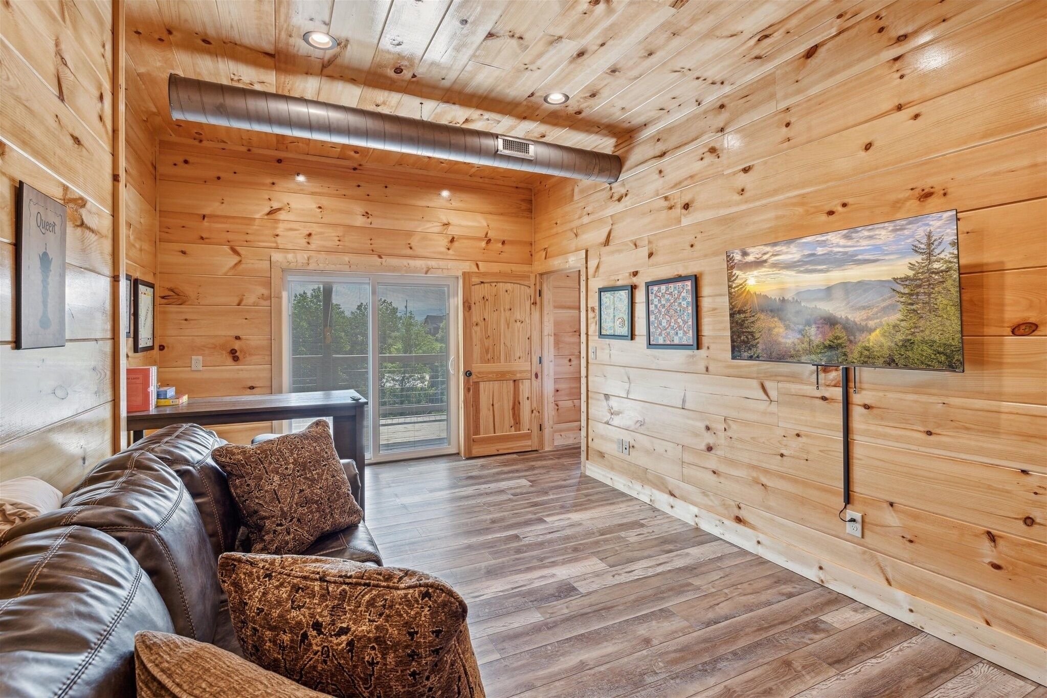 A wooden interior with a leather sofa, framed pictures, and a large window.