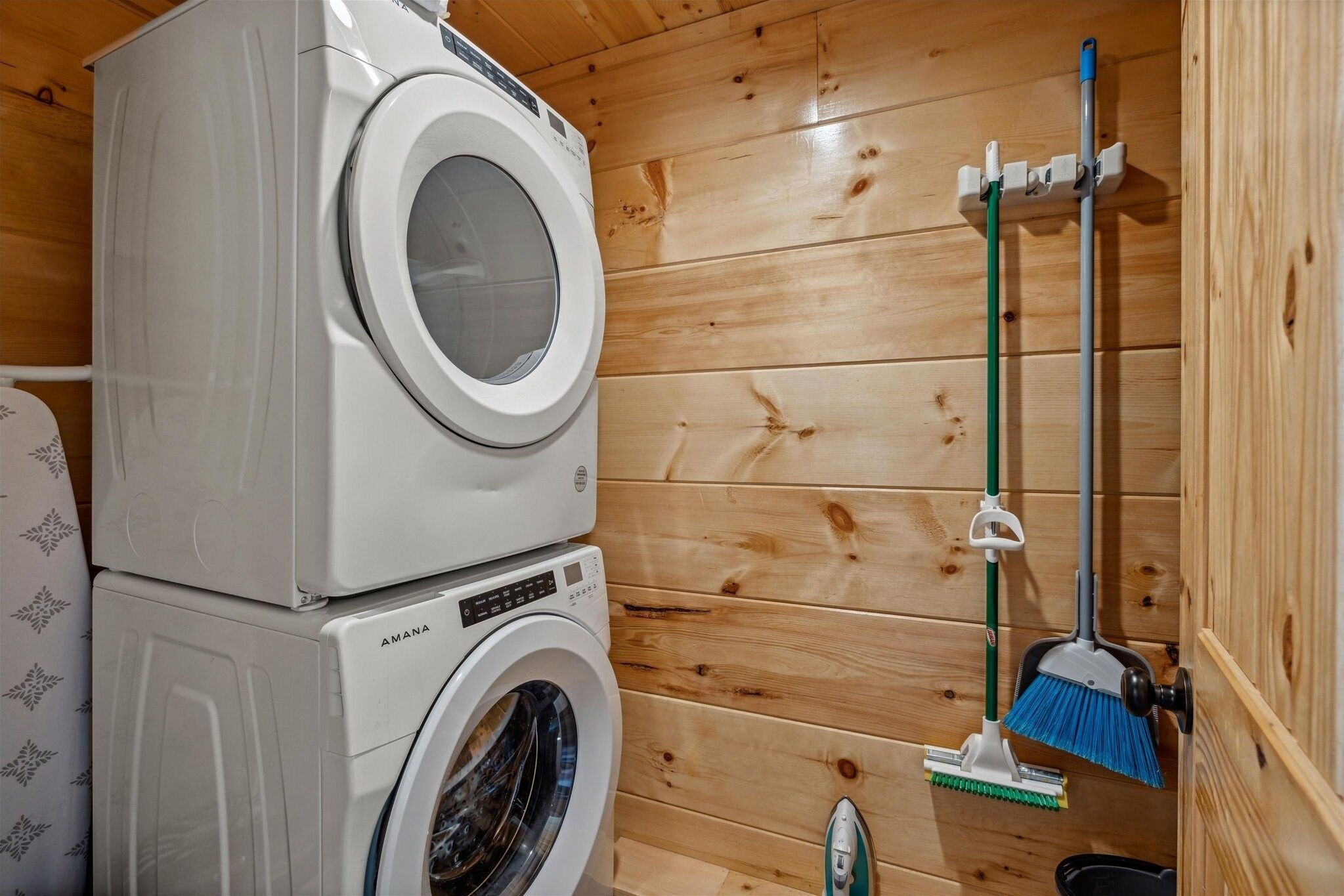 A laundry area with stacked washing machines and a broom leaning against the wall.