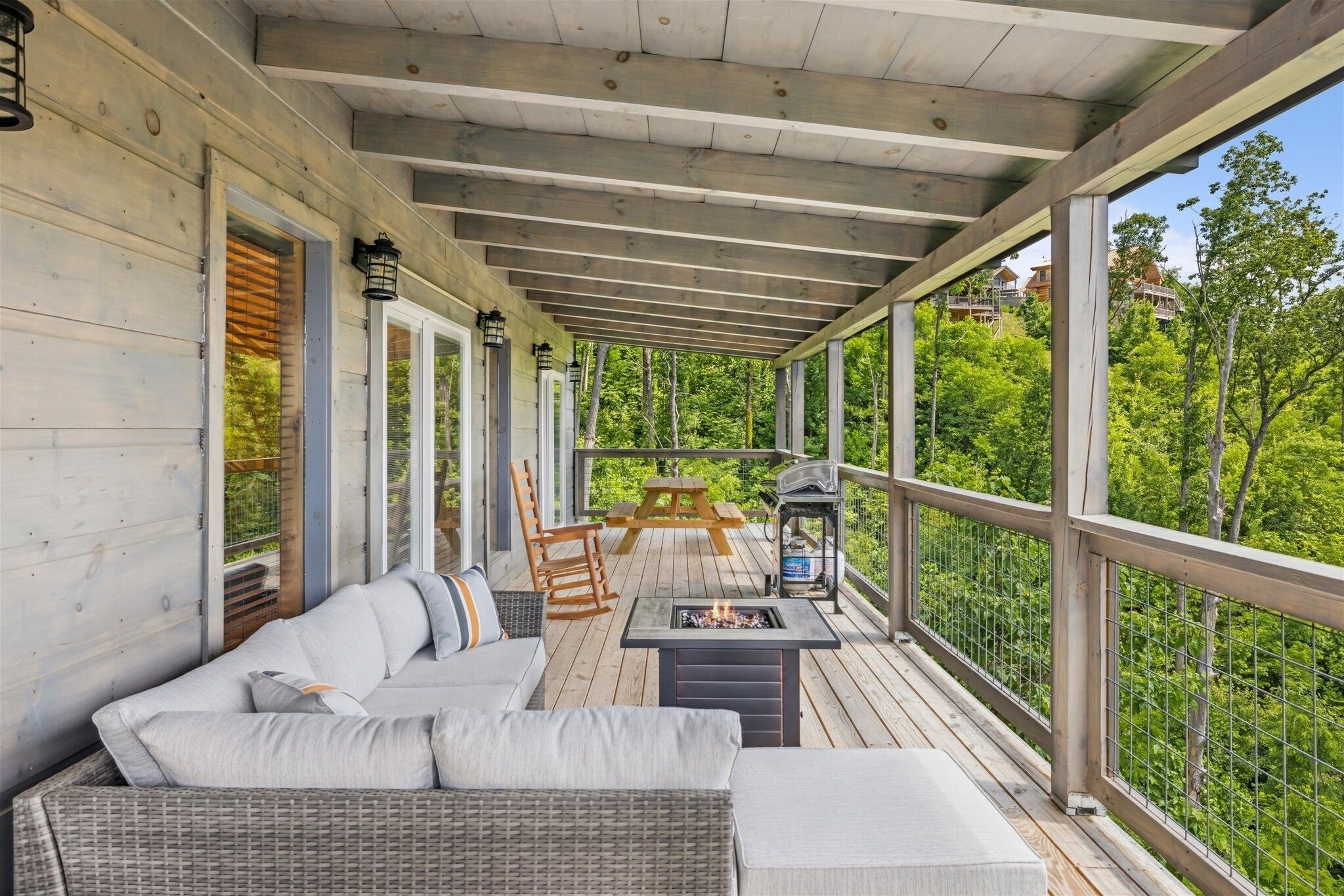A covered outdoor deck with a sofa, chairs, a table, and a fire pit.