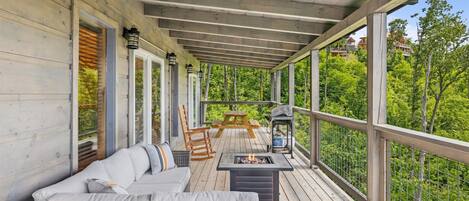 A covered outdoor deck with a sofa, chairs, a table, and a fire pit.