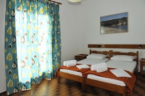 A double bed with white linens, two bedside tables, and a window with a view of a beach.