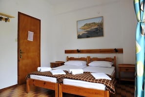 A bedroom with a wooden bed, two bedside tables, a wooden door, and a painting on the wall.