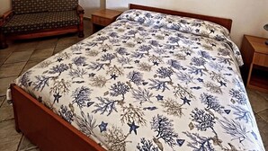A bedroom with a bed, a chair, a small table, and a painting on the wall. - Case Vacanze Le Buganville (Forio)
