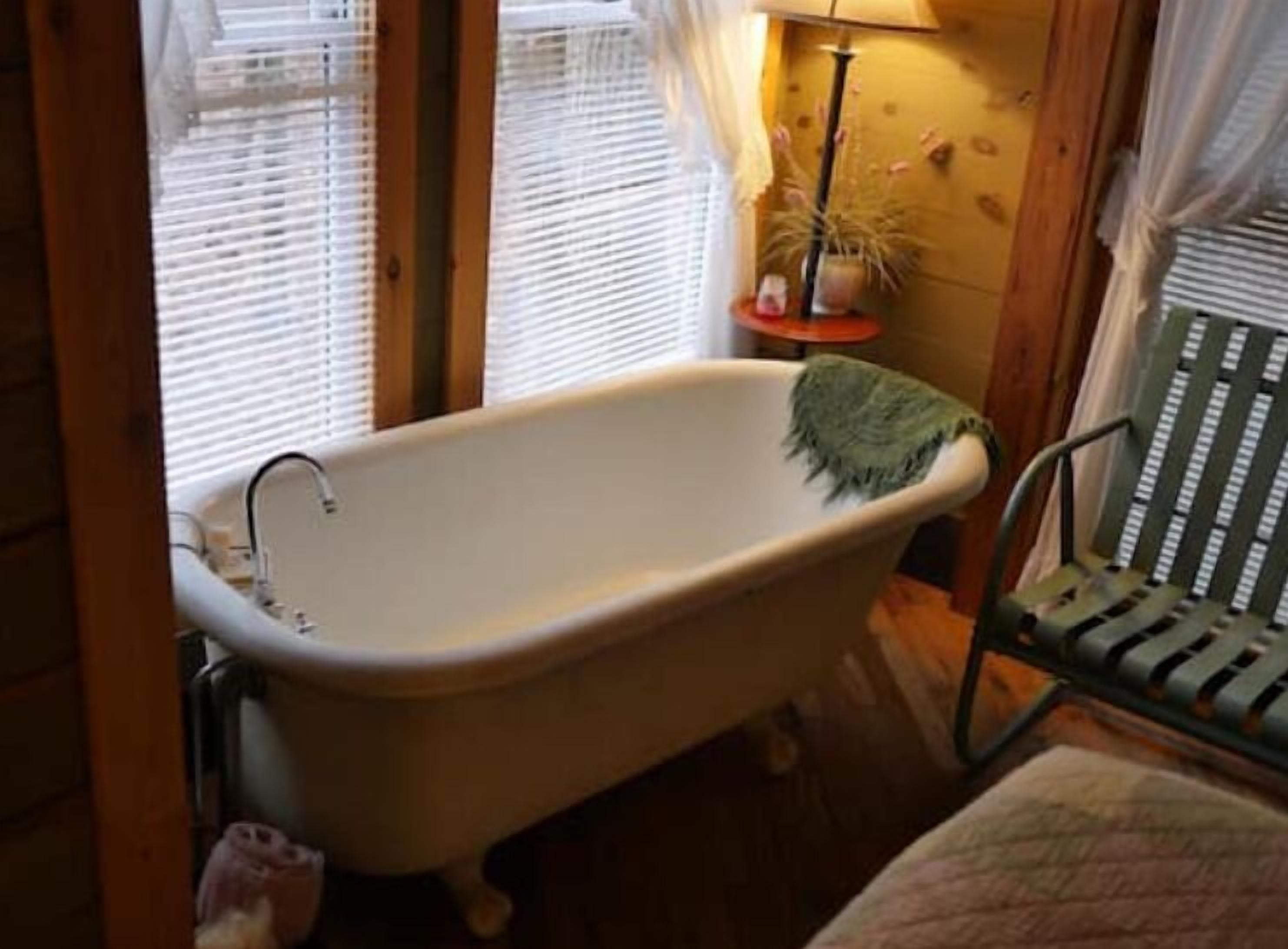 A bathroom with a white bathtub, a green chair, and a small table with a lamp.