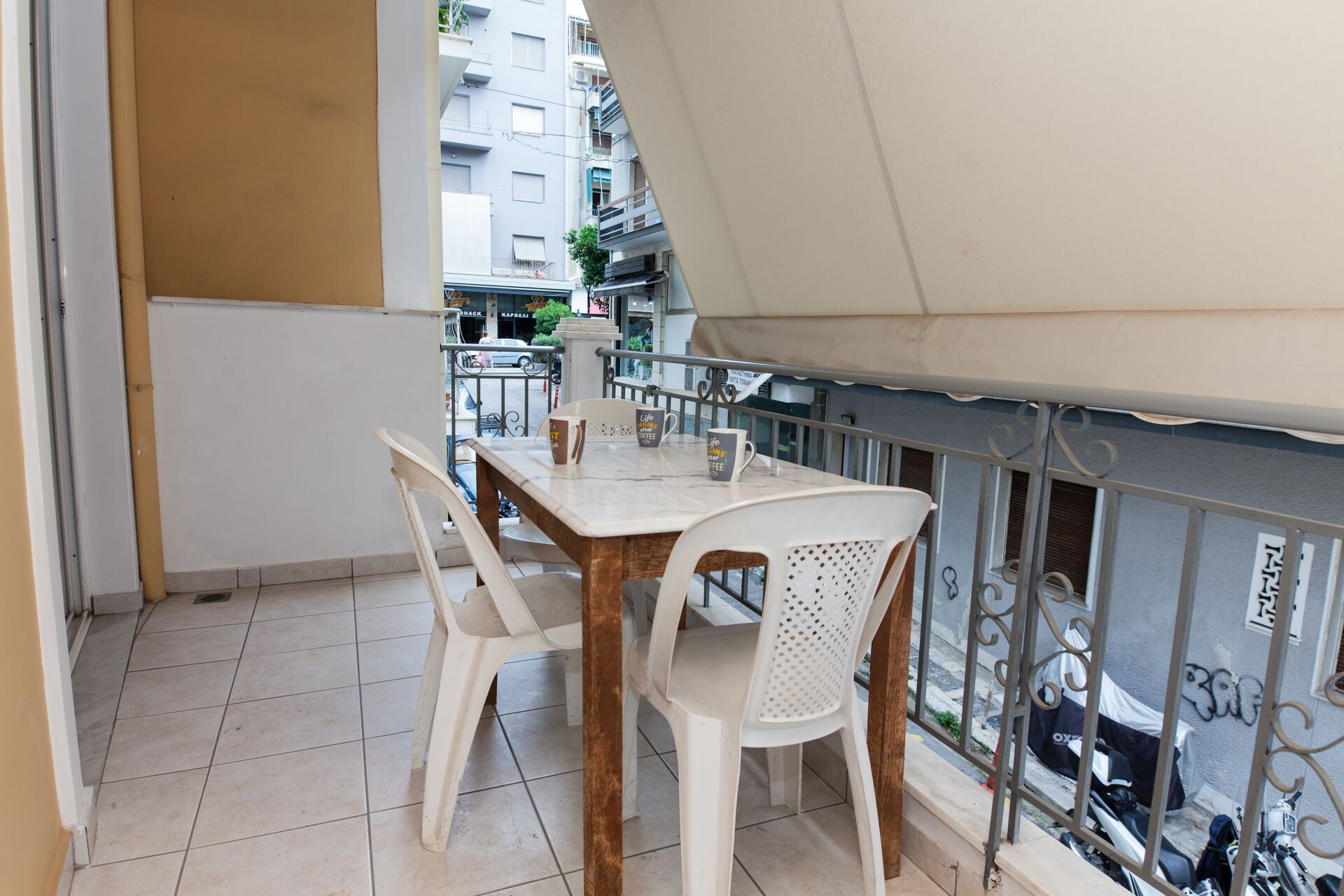 Een balkon met een tafel en stoelen, een uitzicht op de straat, en een gebouw op de achtergrond.