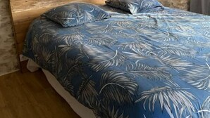 Un dormitorio con pared de piedra, cabecera de madera y cama con colcha azul estampada con flores.