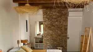 A bedroom with a bed, a stone wall, a wooden ceiling, and a hanging light fixture. - La Ferme '' (Nîmes)