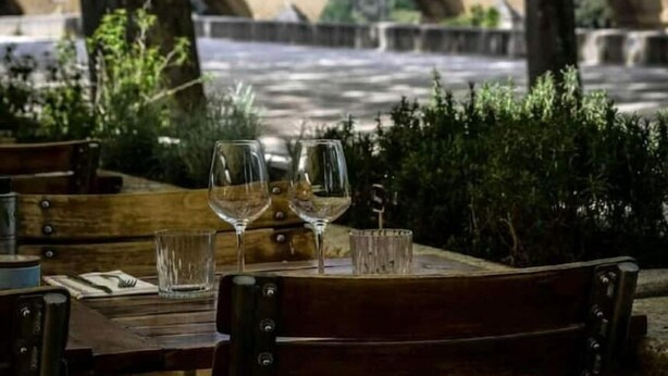 A table with wine glasses and a menu, set against a backdrop of a stone bridge with arches. - La Ferme '' (Nîmes)