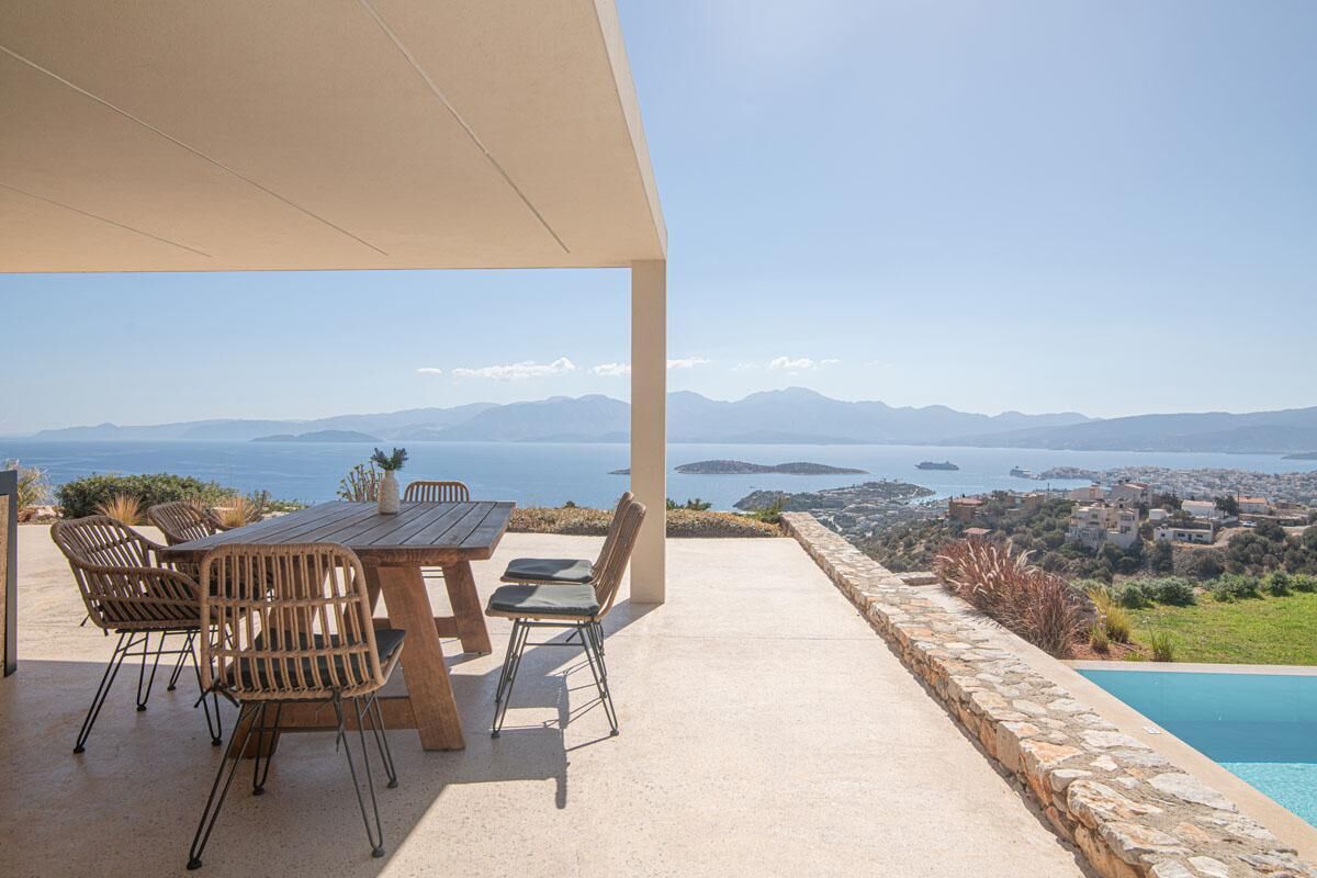An outdoor patio with a table and chairs, overlooking a scenic view of a coastal town and mountains.