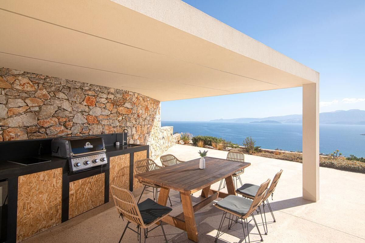 Une terrasse extérieure avec un mur en pierre, un barbecue et une table en bois avec des chaises.