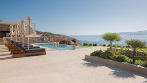 A poolside area with lounge chairs, umbrellas, and a view of the sea. - Horizon View Villa with Endless View (Agios Nikolaos)