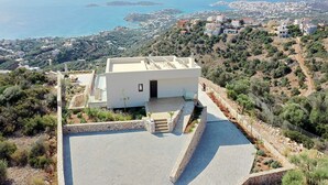 A modern house with a flat roof, a stone retaining wall, and a paved patio. - Horizon View Villa with Endless View (Agios Nikolaos)