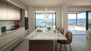 A modern kitchen with a marble countertop, a built-in oven, and a large island with seating. - Horizon View Villa with Endless View (Agios Nikolaos)