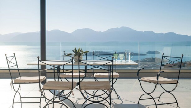 A terrace with a table and chairs, a potted plant, and a view of the sea and mountains. - Horizon View Villa with Endless View (Agios Nikolaos)