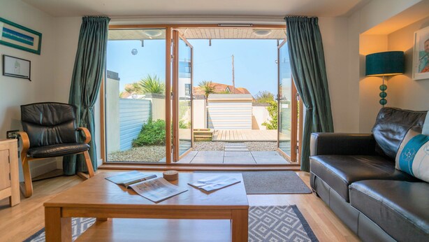 A modern living room with a sofa, a chair, a coffee table, and a sliding glass door leading to an outdoor patio. - Fistral Beach - Apartment 3 (Newquay)