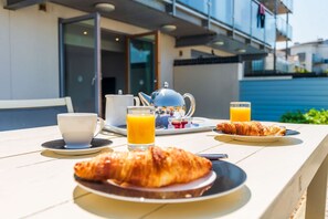 Une table de petit-déjeuner avec des croissants, une tasse, une théière et un verre de jus d’orange.