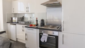 A modern kitchen with white cabinets, a stainless steel range hood, a built-in oven, and a countertop with a kettle and a bottle of wine.