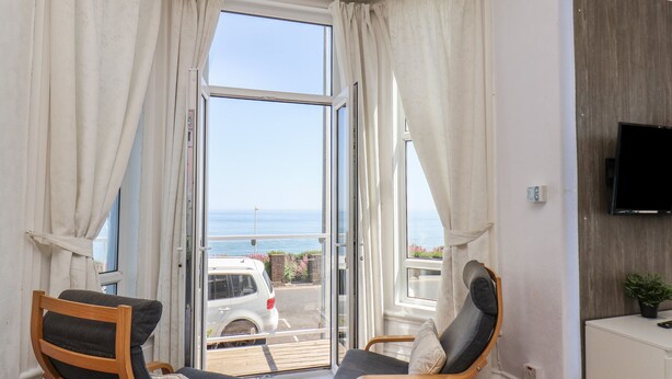 A room with two chairs, a TV, and a view of the sea.