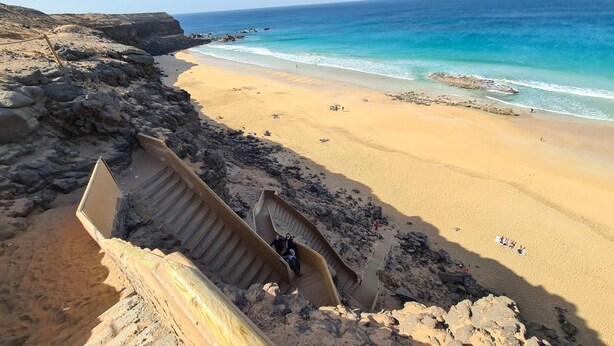 A beach with a rocky cliff and a staircase leading down to the shore. - Casa Fin del Mundo El Cotillo (El Cotillo)