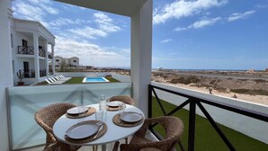 A balcony with a table set for two, overlooking a pool and a beach. - Casa Fin del Mundo El Cotillo (El Cotillo)