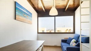 Une pièce avec un plafond en bois, une grande fenêtre donnant sur la ville, un canapé bleu et une table en bois.