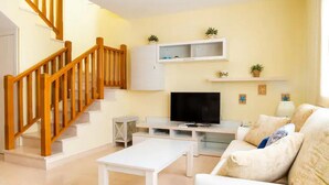 Un salon avec un escalier en bois, un téléviseur à écran plat, un canapé blanc et une table basse.