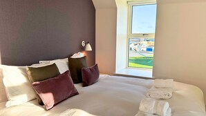 A hotel room with a large bed, pillows, a nightstand with a lamp, and a window with a view of a playground. - Northstar 2 (Wick)