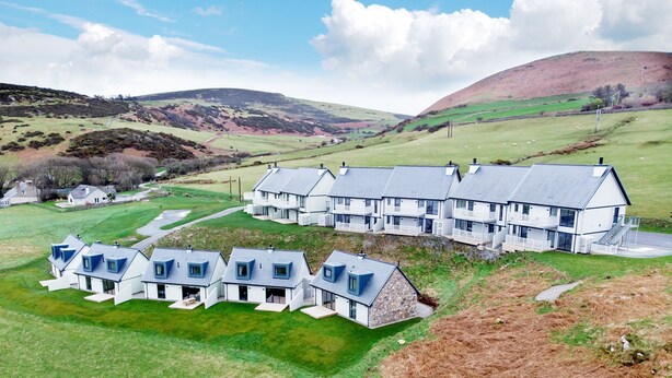 Un complexe résidentiel moderne comprenant plusieurs maisons, une pelouse bien entretenue et un paysage vallonné en arrière-plan.