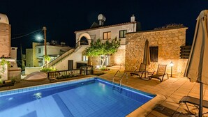 Une piscine bordée d’un mur en pierre et un escalier menant à un deuxième étage.