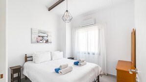 Une chambre d’hôtel comprenant un lit, une table de chevet en bois, un bureau, une chaise, un miroir et une fenêtre avec des rideaux.