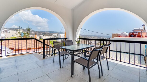 Un balcon avec une table et des chaises, offrant une vue sur le paysage urbain et les collines.