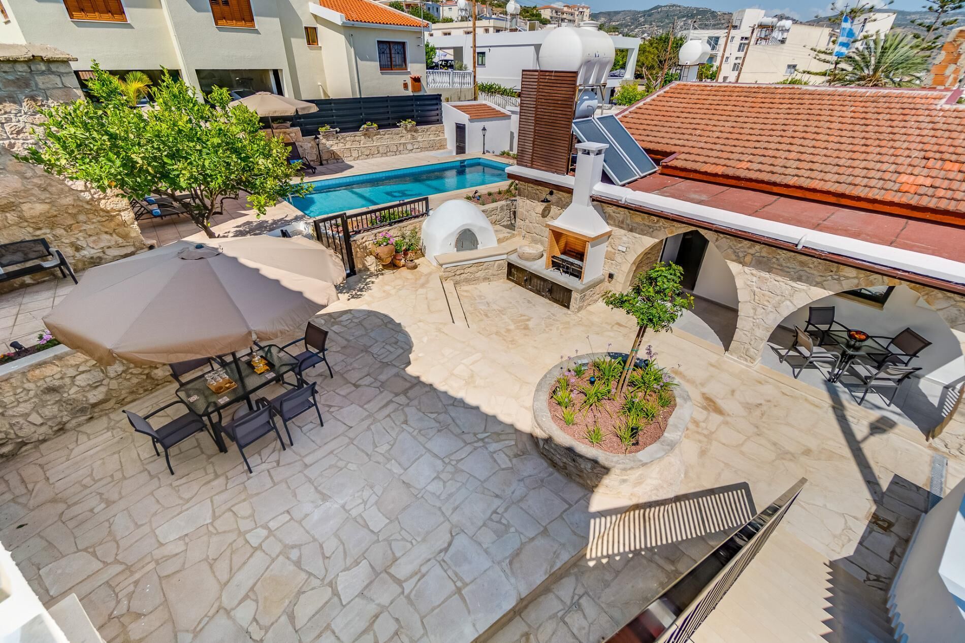 A rooftop pool area with stone flooring, outdoor seating, and a barbecue setup.