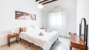 A bedroom with a bed, a bedside table, a lamp, a painting, a window with curtains, and a mirror.