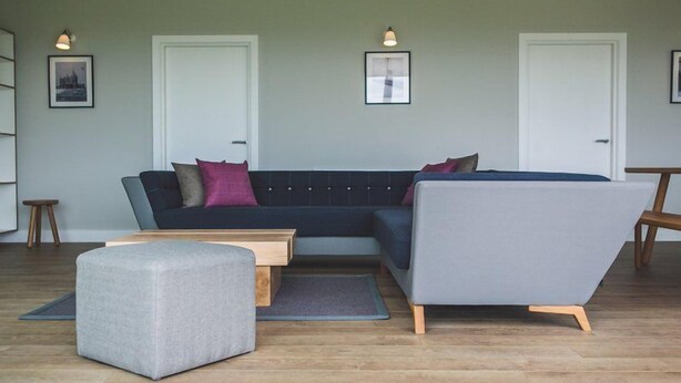 A modern living room with a sectional sofa, a grey ottoman, and a wooden coffee table. There are two doors and two wall-mounted lights. - Jog Lodge 2 - 3 Bed (Wick)