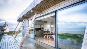 A modern house with a wooden deck, a dining area with a table and chairs, and a kitchen visible through glass doors. - Jog Lodge 2 - 3 Bed (Wick)