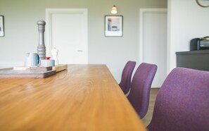 A dining table with a wooden top, surrounded by purple chairs. There are salt and pepper shakers, a white pitcher, and a stack of coasters on the table. - Jog Lodge 2 - 3 Bed (Wick)