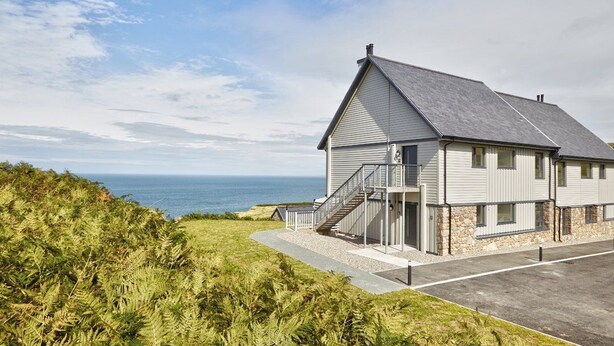 Een huis aan de kust met een stenen fundering, een grijs dak en een trap naar een veranda.