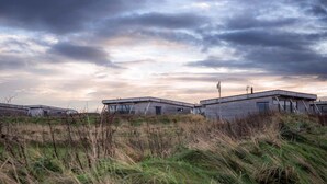 A row of modern, industrial-style buildings with flat roofs and large windows, set against a dramatic sky with clouds. - Jog Lodge 13 - 3 bed (Wick)