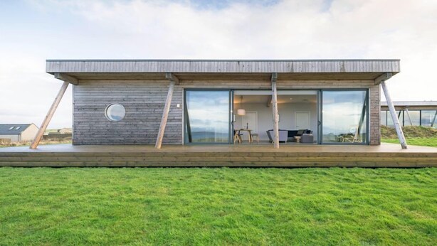 A modern house with a flat roof, large glass windows, and a wooden deck. - Jog Lodge 13 - 3 bed (Wick)