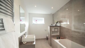 A modern bathroom with a large bathtub, a sink, a mirror, and a window with a flower. - Jog Lodge 13 - 3 bed (Wick)