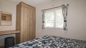 Une chambre à coucher comprenant un lit, une armoire en bois, un bureau et une fenêtre avec des rideaux.