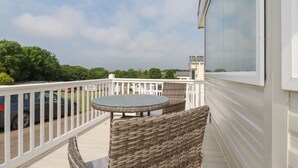 Un balcon avec une table ronde et des chaises en osier, donnant sur un parking et sur un espace verdoyant.