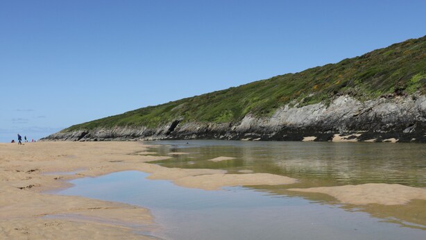 Une plage à l’eau claire, bordée d’une falaise rocheuse.