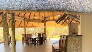A covered outdoor dining area with stone pillars, wooden tables and chairs, and a stone counter.