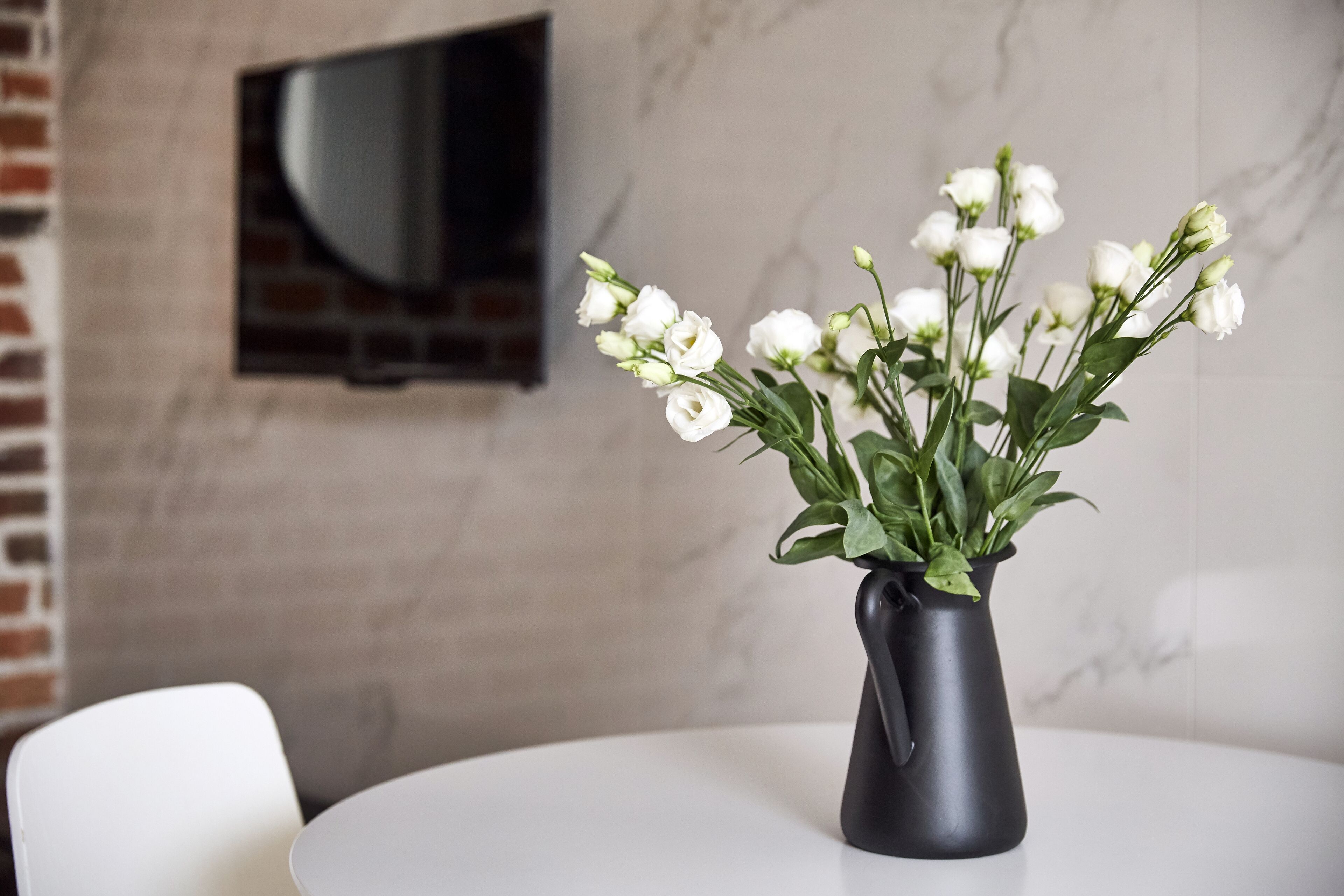 Ein weißer Tisch mit einer schwarzen Vase und weißen Blumen.
