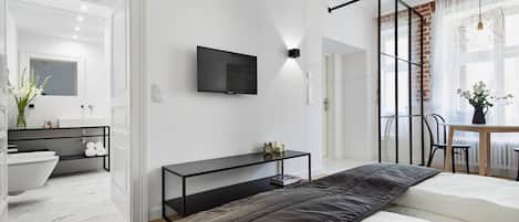 A modern bedroom with a bed, a TV, a bedside table, and a bathroom with a sink and mirror.