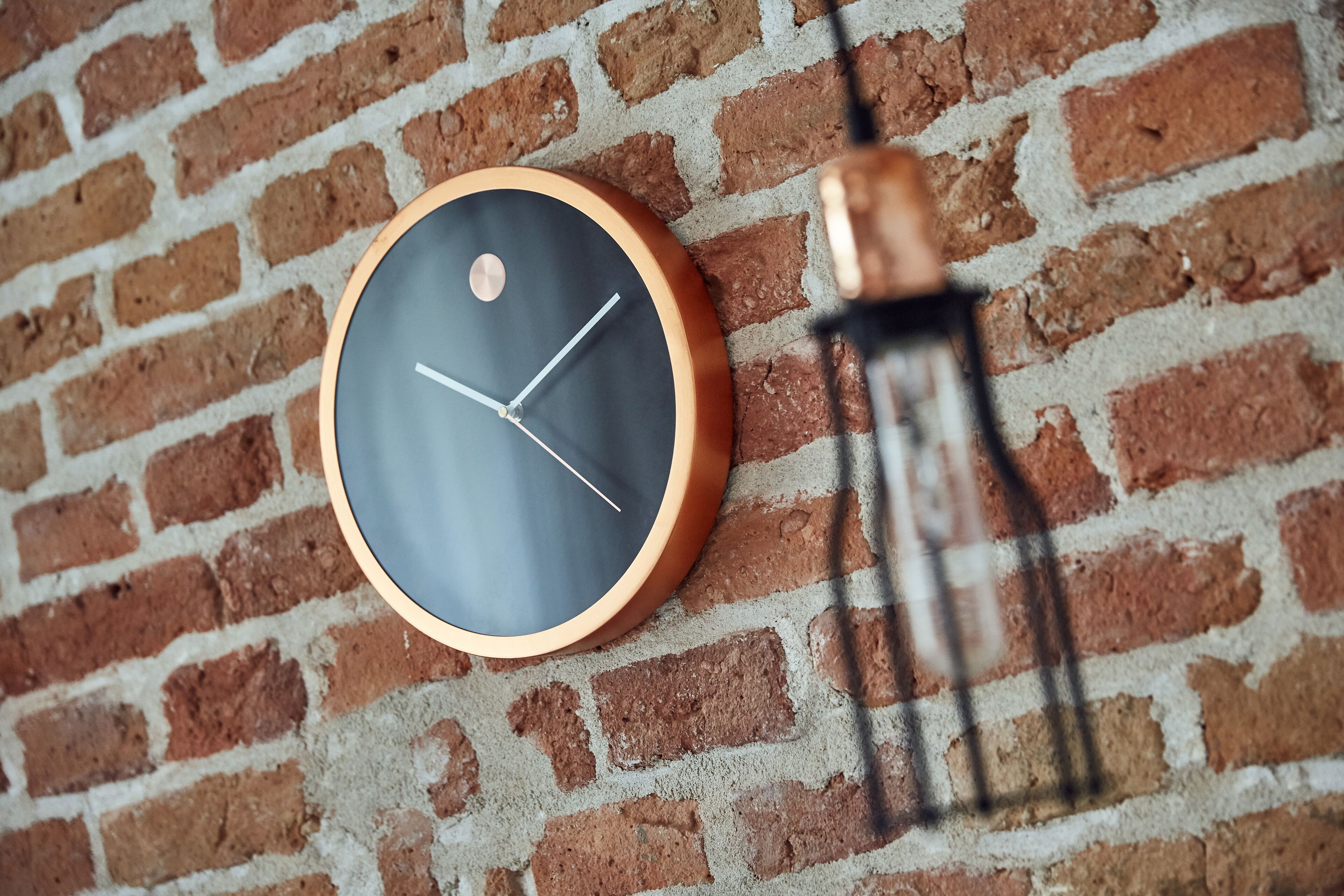 A round wall clock with a copper frame on a brick wall.